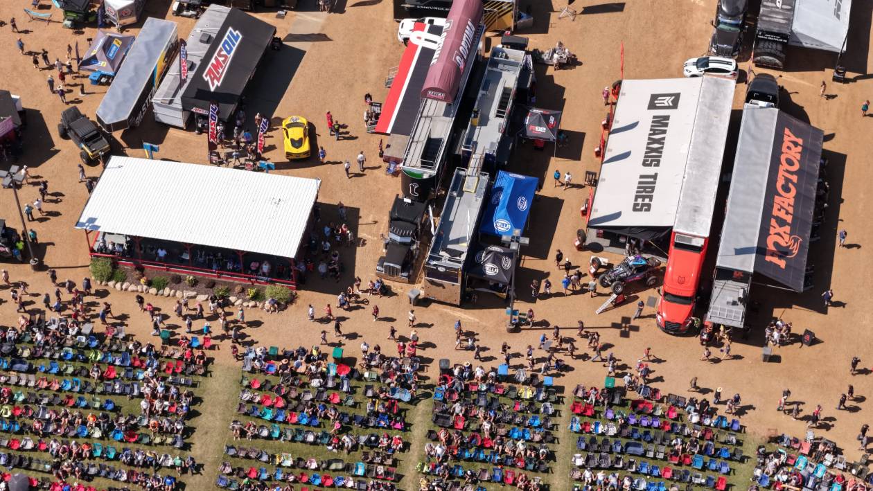Aerial view of the vendor row at Crandon, with branded trailers, display vehicles and rows of spectators in lawn chairs