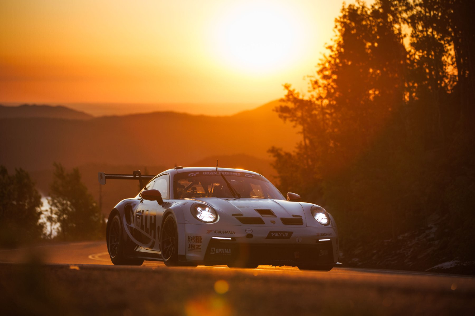 White race car with headlights on, climbing the Pikes Peak Highway at sunrise
