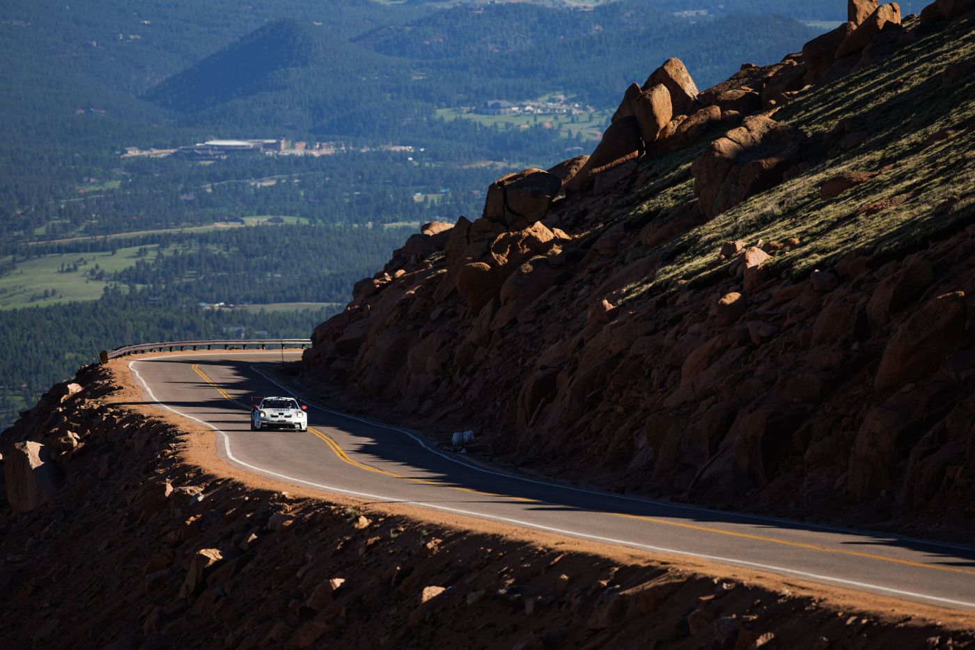 Race car on a shaded mountain road high above the forested valley at Pikes Peak